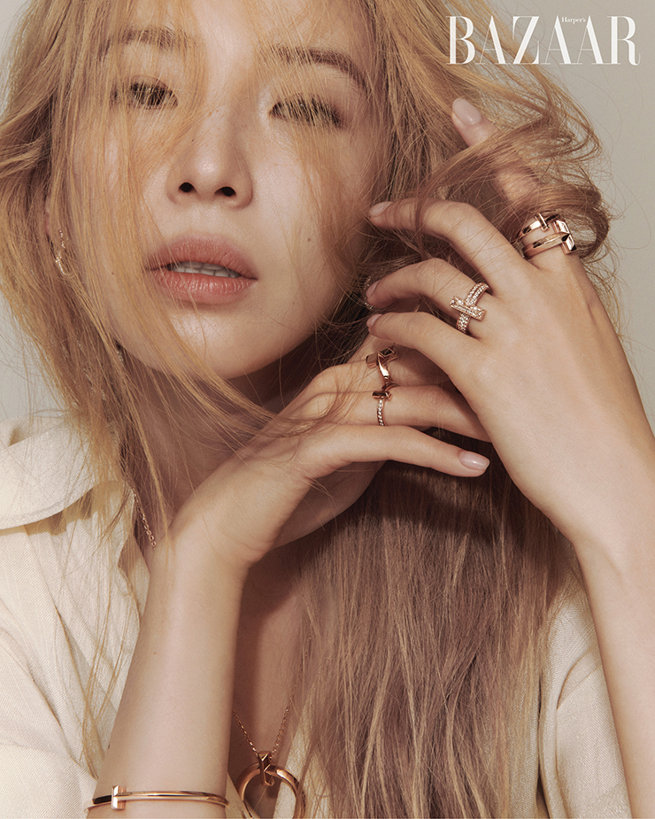 18K 로즈 골드에 브릴리언트 다이아몬드가 장식된 ‘티파니 T1 오픈 후프’ 이어링, 18K 로즈 골드 ‘티파니 T1 라지 써클 펜던트’ 네크리스, 18K 로즈 골드 ‘티파니 T1 내로우 힌지드’ 뱅글, 오른손 중지에 낀 18K 로즈 골드 ‘티파니 T1 와이드 하프 다이아몬드’ 링, 약지에 낀 ‘티파니 T1 내로우 하프 다이아몬드’ 링, 왼손 약지에 낀 18K 로즈 골드 ‘티파니 T1 와이드 풀 다이아몬드’ 링, 검지에 낀 18K 로즈 골드 ‘티파니 T1 내로우’ 링, ‘티파니 T1 와이드 바게트 컷 다이아몬드’ 링은 모두 Tiffany & Co.. 셔츠는 Lvir.